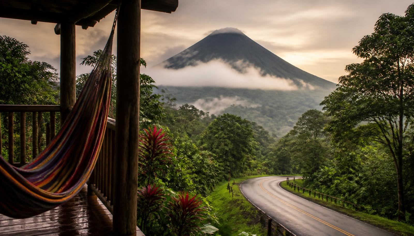 Winding road through misty Costa Rican cloud forest with a volcano behind and a hammock on a lodge porch